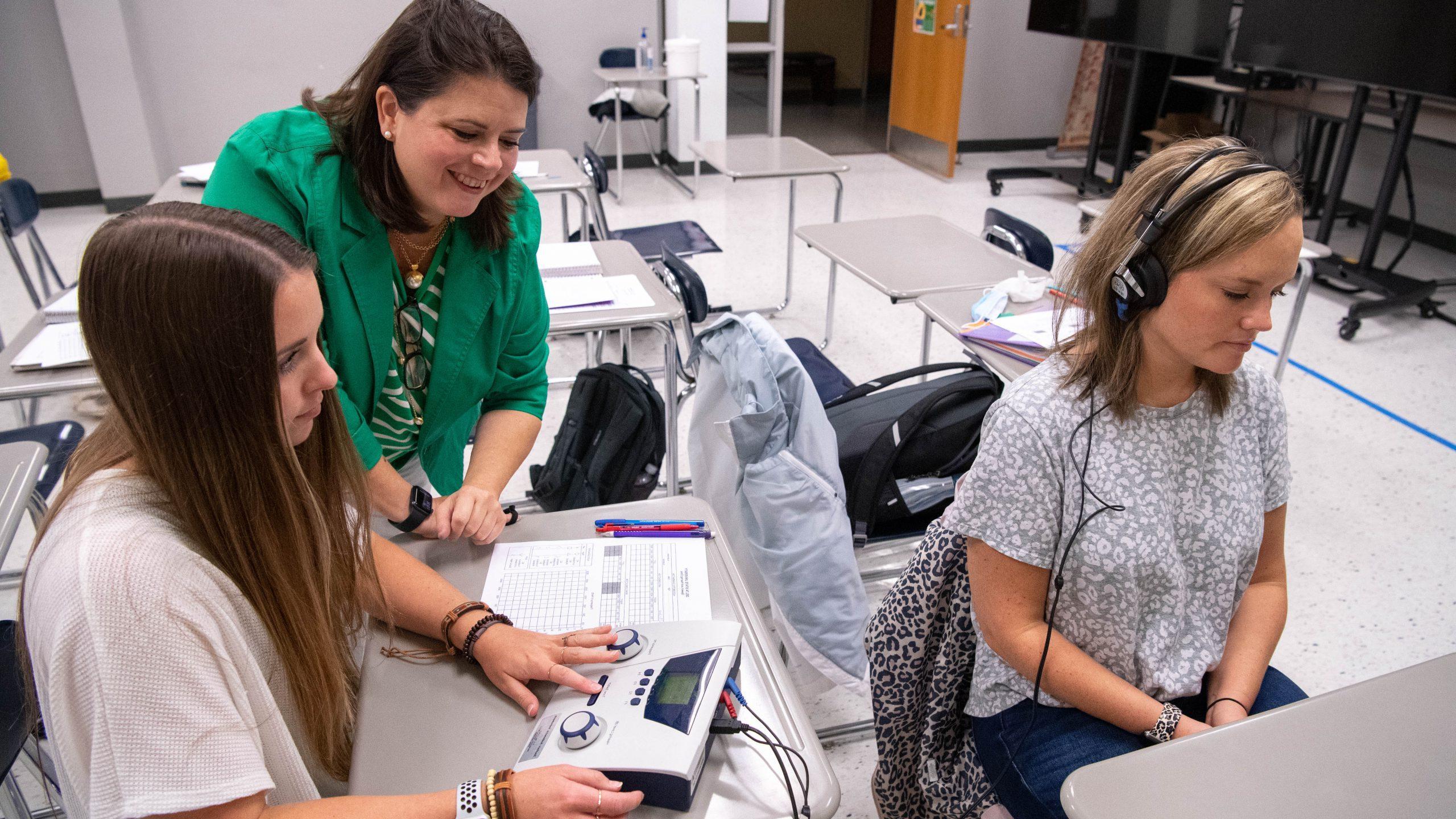 Instructor and student conducting hearing test on another student in a classroom setting.